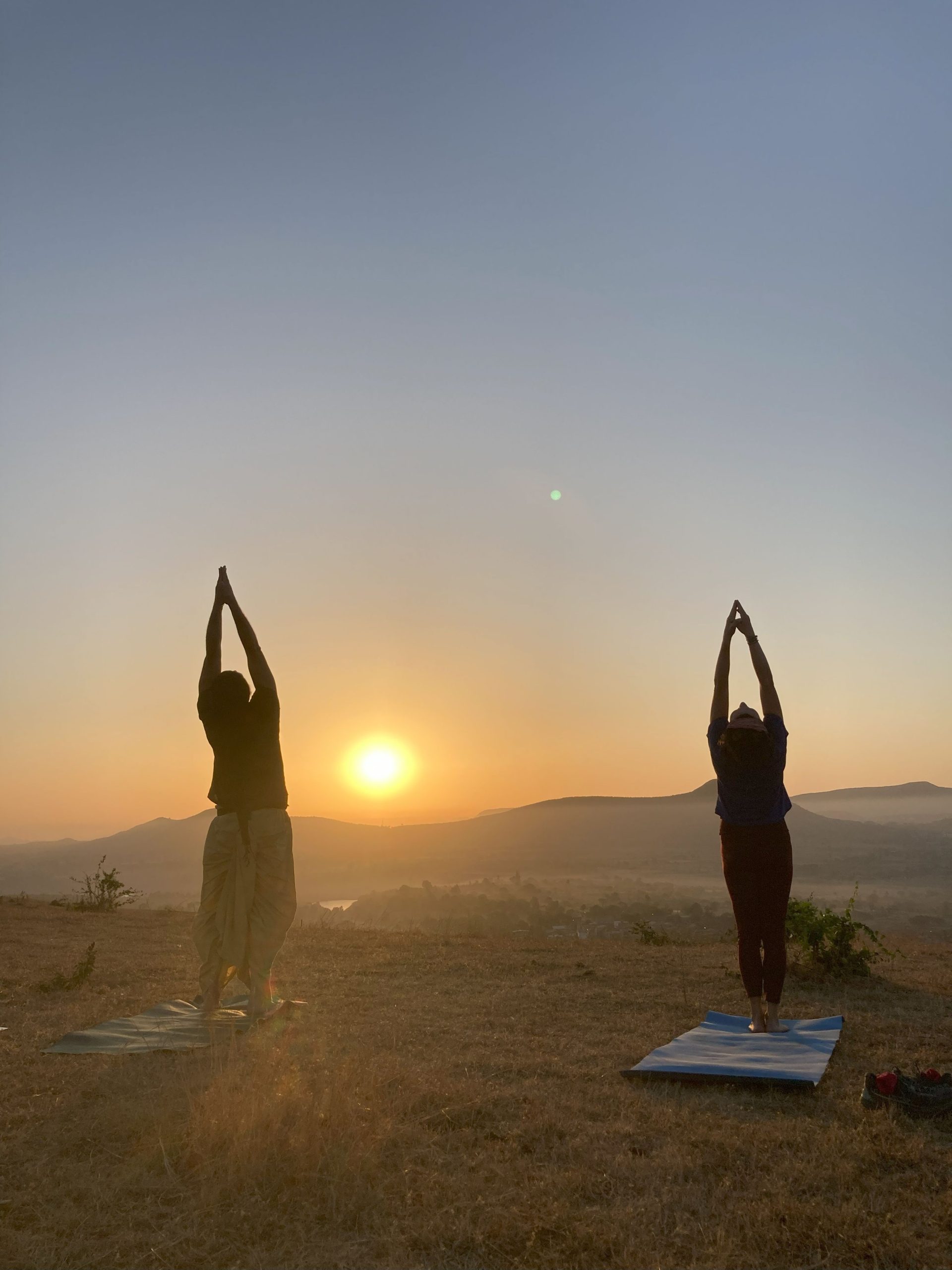 Due persone eseguono il saluto al sole yogico all'alba su una collina