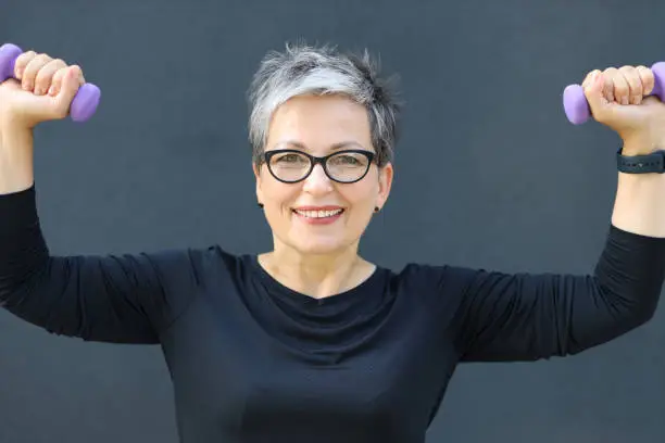 Donna senior che solleva due pesi con espressione sorridente
